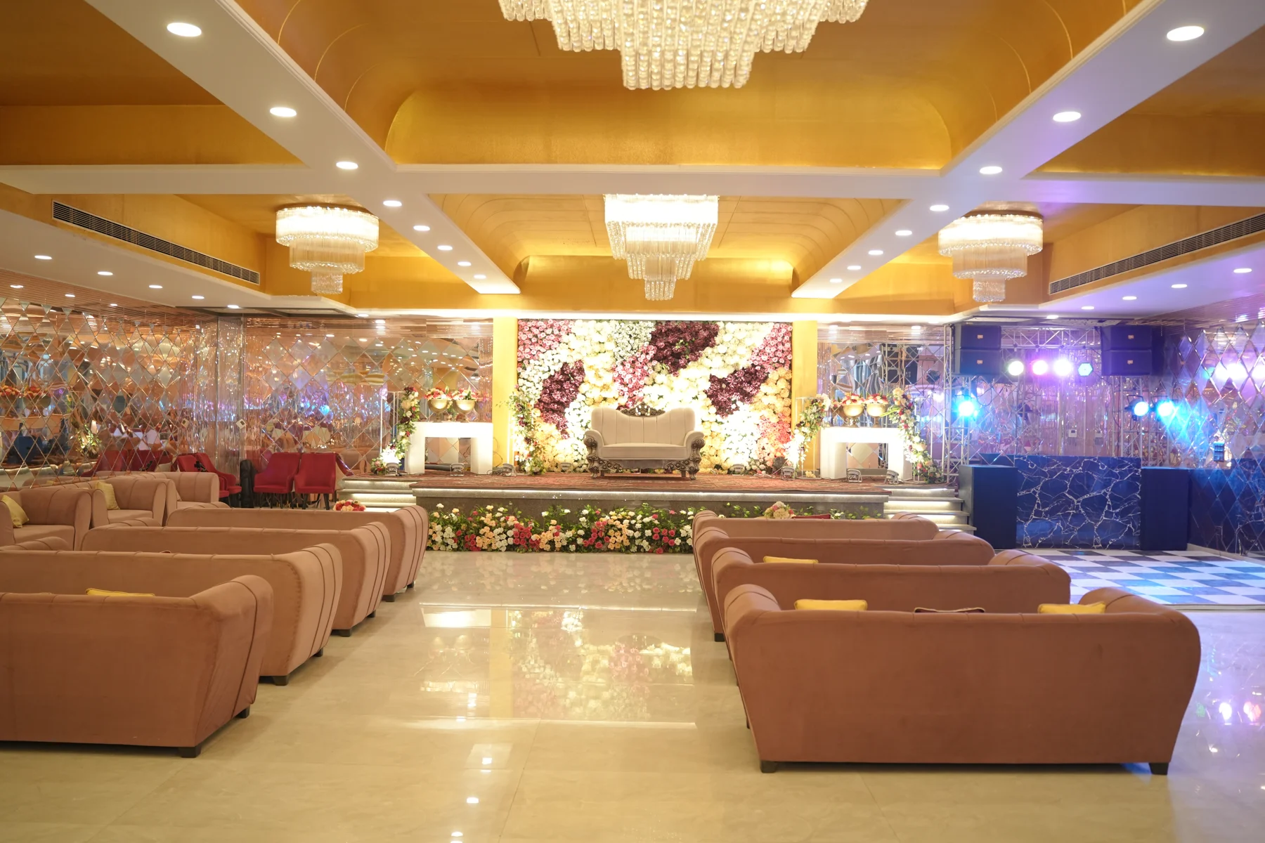 Banquet hall with gold ceiling, seating and floral stage at Clubex Banquets & Lawns